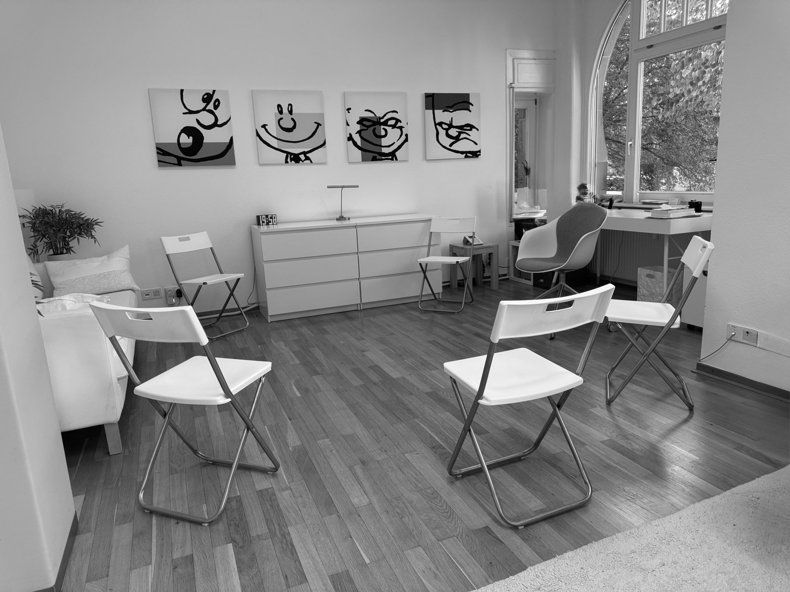Derselbe Raum für eine Gruppe vorbereitet: Stühle stehen im Kreis, an der Wand vier Bilder mit gezeichneten Gesichtern.